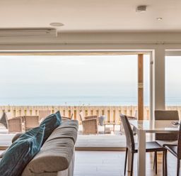 A living room with a sofa and dining table opening to an outdoor deck with seating and ocean view at Boscarne in St Ives