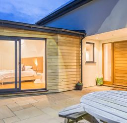 An outdoor patio with wooden round table and a bedroom visible through large glass doors at Boscarne in St Ives