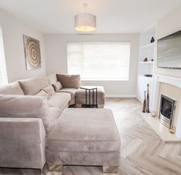 A living room with a beige sectional sofa a fireplace a wall-mounted television and wooden floor at 4 Bodnant Road Rhos-On-Sea