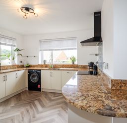 A kitchen with granite countertops a black washing machine a microwave and plants on windowsills at 4 Bodnant Road in Rhos-On-Sea