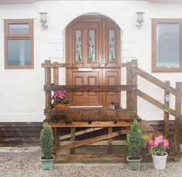 Front entrance of a house with wooden double doors a porch with railings two potted plants on the ground and flowering plants on the porch at The Dovecote in Hartland