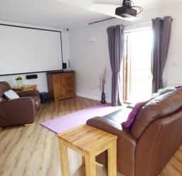 A living room with leather sofa and armchair a projector screen and wooden furniture at Penylodge in Builth Wells