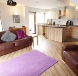 An open living room and kitchen with brown leather sofas purple cushions a purple rug and wooden flooring at Penylodge in Builth Wells