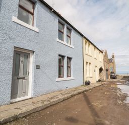 A row of houses along a dirt street with puddles including a blue house with a gray door and a yellow house at Sunnie Cottage in Seahouses