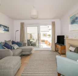 A living room with a grey sofa and ottoman a blue armchair television fireplace and sliding glass doors leading outside at 5 Ocean Heights in Newquay