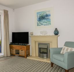 A living room with a fireplace TV on a wooden stand an armchair and a painting of a wave at 5 Ocean Heights in Newquay