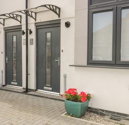 Two dark grey front doors with canopies and a green planter with red flowers outside a building at 5 Ocean Heights in Newquay