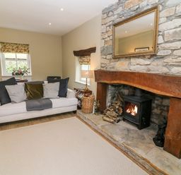 A living room with a fireplace wooden beam mantel white sofa cushions and wooden floor at Waingate Cottage in Flookburgh