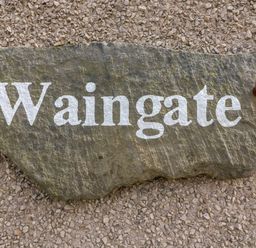 A stone plaque with the word Waingate mounted on a textured wall at Waingate Cottage in Flookburgh
