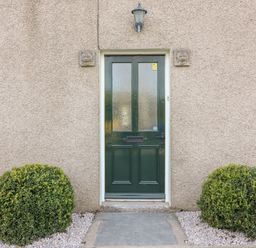 A green front door with frosted glass panels flanked by two bushes at Waingate Cottage in Flookburgh