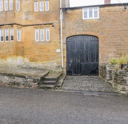 An exterior view of a stone building with multiple windows and a large black wooden gate at Bower Coach House in Bower Hinton near Martock