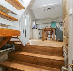 View of wooden stairs leading to a kitchen dining area with a wooden chair a grey sofa and white cabinets at Bower Coach House in Bower Hinton near Martock