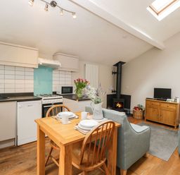 An open kitchen and living area with a wooden dining table set for two a wood burning stove and a small TV on a wooden cabinet at Bower Coach House in Bower Hinton near Martock