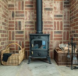 A wood stove with firewood baskets and tools at East Wing in Crewkerne