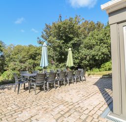 An outdoor patio with a long dining table surrounded by chairs and two closed umbrellas at Ros Vale in St Buryan