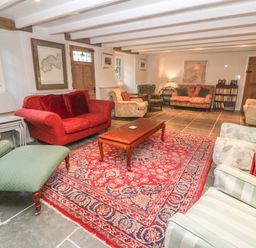 A living room with multiple armchairs and sofas around a wooden coffee table on a patterned rug at Ros Vale in St Buryan
