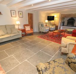 A living room with various chairs and sofas a red patterned rug a fireplace and a wall clock at Ros Vale in St Buryan