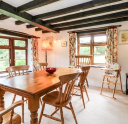 A dining room with a wooden table and chairs near windows with floral curtains at Meadow Lea Pensilva near Liskeard