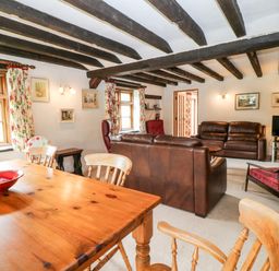 A living room and dining area with wooden table chairs leather sofas and exposed wooden beams at Meadow Lea in Pensilva near Liskeard