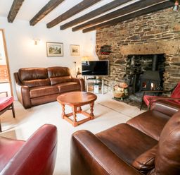 A living room with leather sofas stone fireplace wooden beams and a television at Meadow Lea in Pensilva near Liskeard