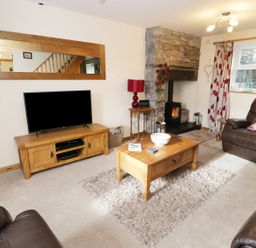 A living room with a television on a wooden stand a coffee table on a rug leather armchairs a stone fireplace and patterned curtains at 60 Hyfrydle Road Talysarn near Caernarfon