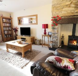 A living room with a stone fireplace a wood stove and a wooden coffee table at 60 Hyfrydle Road in Talysarn near Caernarfon
