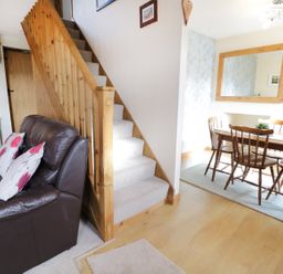 A living room with a brown leather sofa and wooden stairs next to a dining area with a wooden table and chairs at 60 Hyfrydle Road Talysarn near Caernarfon