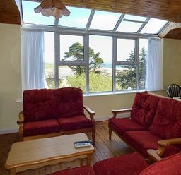 A living room with red cushioned sofas and a wooden coffee table in front of large windows overlooking trees at Number 12 Mulranny County Mayo