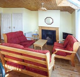 A living room with wooden ceiling red cushioned sofas coffee table fireplace and large window at Number 12 Mulranny County Mayo