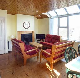 A living room with wooden sofas and a fireplace by large windows at Number 12 in Mulranny County Mayo