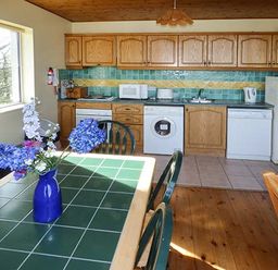 A kitchen with wooden cabinets and appliances beside a dining table with a vase of flowers at Number 12 in Mulranny County Mayo