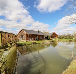 Cabins near a pond with a wooden bridge and trees at Lily-pad Lodge in Thorpe-on-the-Hill