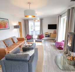 A living room with a leather sofa gray armchairs a wood burning stove and a wall mounted TV at Lily-pad Lodge in Thorpe-on-the-Hill