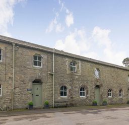 A stone building with multiple green doors and windows along a paved road at Gardeners Cottage in Bellingham