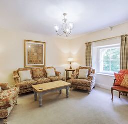 A sitting room with patterned sofas a wooden coffee table and a window with curtains at Gardeners Cottage in Bellingham