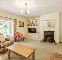 A living room with patterned armchairs a wooden coffee table fireplace and a built in bookshelf with a tv at Gardeners Cottage in Bellingham