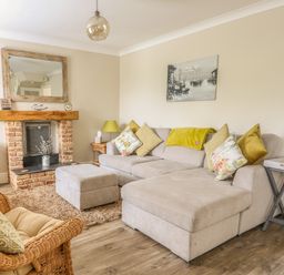 A living room with a beige sofa and cushions a wicker chair a brick fireplace and a television at Bertelle in Grimston