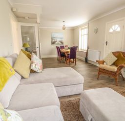 A living room with a grey sofa, a wicker chair with cushions, and a dining table with purple chairs at Bertelle in Grimston