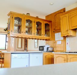 A kitchen with wooden cabinets a microwave a toaster and a dining table with chairs at Flynn's Cottage in Quilty County Clare