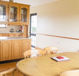 A dining area with a wooden table and chairs next to a kitchen with wooden cabinets and a black door at Flynn's Cottage in Quilty County Clare