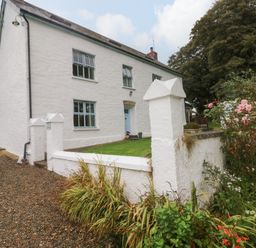 A white two-story house with blue windows and a blue door surrounded by a white wall and garden at Ty Llwyd Nevern near Cardigan