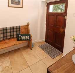 An entryway with a wooden bench holding a plaid blanket and a Croeso pillow a wooden door a striped doormat and a wooden table with a vase of flowers at Ty Llwyd in Nevern near Cardigan