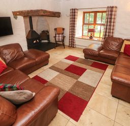 A living room with brown leather sofas a patterned rug a wood stove and a window with plaid curtains at Ty Llwyd in Nevern near Cardigan