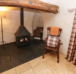 A corner of a room with a wood-burning stove a wooden chair with cushions a floor lamp and a plaid curtain at Ty Llwyd in Nevern near Cardigan