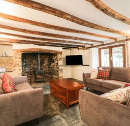 A living room with exposed wooden beams stone fireplace with wood burner sofas and a wooden coffee table at Lower West Curry Farmhouse in Launceston