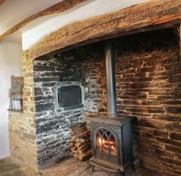 A wood burning stove with firewood in a stone fireplace at Lower West Curry Farmhouse in Launceston