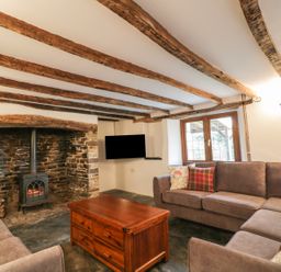 A living room with wooden ceiling beams a stone fireplace wood stove two sofas a wooden coffee table and a wall mounted TV at Lower West Curry Farmhouse Launceston