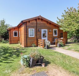 A wooden cabin with white framed windows and a small porch in a grassy garden with trees at Aurora Skies in Cresswell near Morpeth