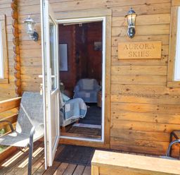 A wooden cabin entrance with an open door two chairs and a sign reading Aurora Skies at Aurora Skies in Cresswell near Morpeth