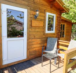 A wooden cabin entrance with a white door two chairs and a small table on the porch at Aurora Skies in Cresswell near Morpeth